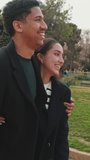 Vertical video, Happy couple sharing playful moment and embracing outdoors in park setting.