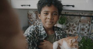 Portrait of African American kid making online video call speaking showing kitten looking at camera in kitchen at home. Communication and childhood concept.