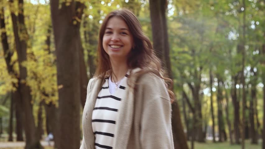 Woman walking outdoor, young european lady in warm sunny autumn city park season, fall, hold yellow orange red leaves, lifestyle, spending free time

