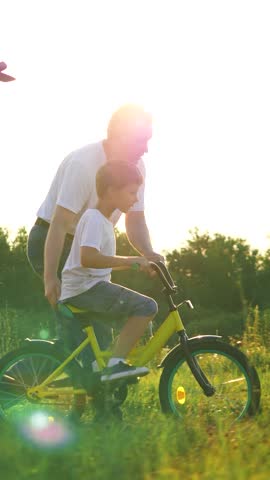Happy family of father son and daughter spend active weekend together in summer field. Father helps son on bicycle and daughter runs nearby in sunny meadow. Father with children play in wild park Royalty-Free Stock Footage #3466461471