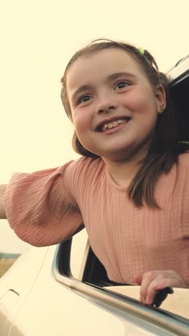 Smiling little girl pulls hand out of car window travelling across farmland in summer evening. Little girl happy of journey leans out of car window. Girl enjoys road trip by car at countryside Royalty-Free Stock Footage #3466462197