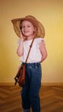 Cute girl in hat laughing on phone call. Little girl in straw hat talking excitedly on phone. Vertical video. Young girl in sun hat chatting on cellphone. Child in straw hat having lively phone conver