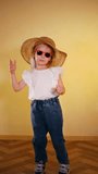 Smiling girl in sunglasses and straw hat dances funny. Fashionable little girl with stylish summer accessories. Cute girl enjoying sunny day. Happy child in trendy summer attire