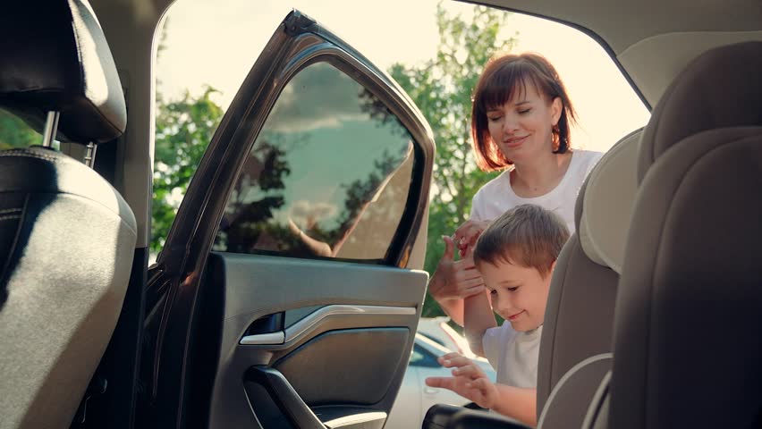 Mother secures her son in car seat using child safety belt. Family road trip. Mom cares about her sons safety. Child sits in car child seat. Mom puts her Kid son in car seat, safe car. Happy family. Royalty-Free Stock Footage #3466495409