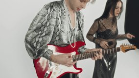 Cropped side footage of unidentified male bassist energetically playing electric bass guitar while performing rock song with indie band on white background in studio