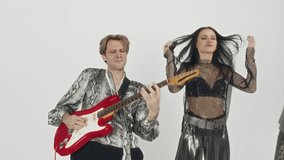 Medium footage of Caucasian bass player rocking out with front woman while recording music clip in professional studio with white background