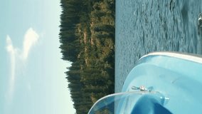 Electric boat sailing on mountain lake. Blue tourist ship floating on water along lake with green trees and hills on background. Vertical video