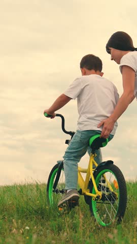Mom teaches her little son to ride bicycle, on meadow. Childhood dream to ride bike. Young mother teaches child to keep balance while sitting on bicycle. Happy family life mom boy, Parental support. Royalty-Free Stock Footage #3466534035