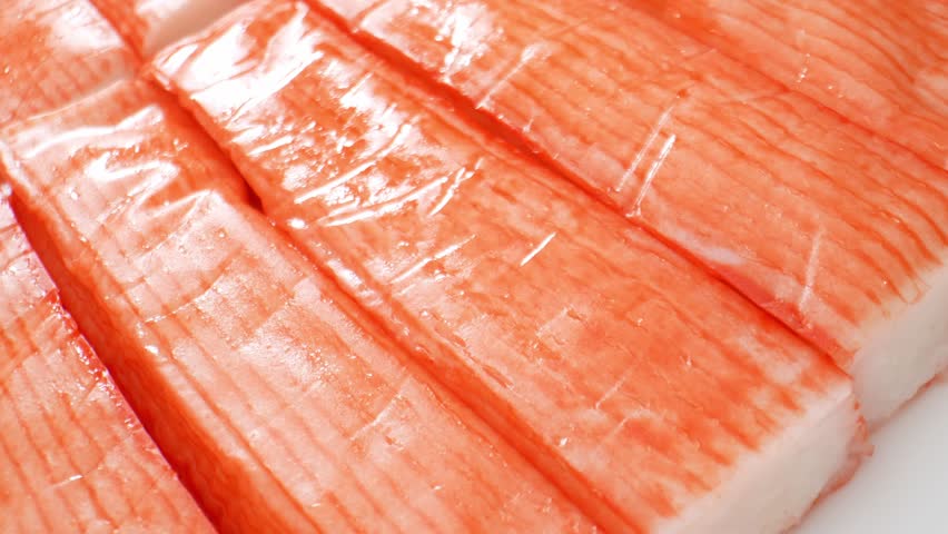 To make crab sticks, white fish is ground into paste, mixed with starch, egg whites, sugar, salt, and flavorings, formed into shapes, steamed or boiled, cooled, and packaged. Crab sticks background.
