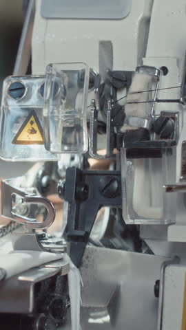 Vertical closeup of hands of unrecognizable seamstress using sewing machine that making seams on piece of fabrics and cutting material indoors