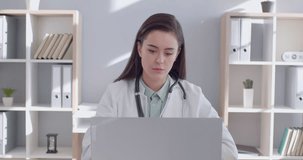 Young confident female doctor working at the desk on her workplace at office talking by mobile phone consulting sick patients and looking at laptop monitor screen in medical clinic. 4k video.