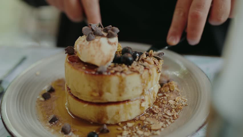 Cropped view on man eating delicious japanese pancake with syrup and blueberry for breakfast at cafe. Male hands cutting sweet fluffy pancake with honey and berry at restaurant