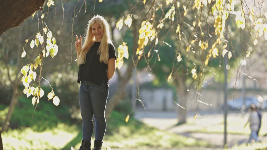 A woman is standing on a tree branch and is holding up her hands in a peace sign
