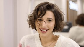 happy woman with short brunette hair sitting in hairdressing cape in beauty salon, getting haircut by professional hairdresser.girl doing keratin treatment.curls at the end.wet hair,towel on head.4k - Powered by Shutterstock - Get 15% off with code: PIKWIZARD15