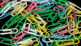 Colorful office clips isolated on black background, stationery supplies. Multicolored rotating paper clips close up