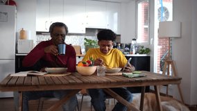 An older man and a boy chat while eating a nutritious breakfast. Watch videos on your smartphone. Grandfather and Grandson Sharing a Healthy Breakfast in Kitchen, watching social media. - Powered by Shutterstock - Get 15% off with code: PIKWIZARD15