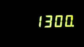 Slow-motion shot, yellow LCD digits glow against a dark background, displaying the number 1300. Evokes a clock suspended into a dream or a score in a video game.