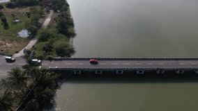 A striking aerial video showing a red car driving on a highway bridge next to the sea and backwaters Chennai East coast road.