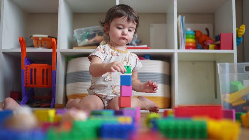 baby plays with toy blocks on floor. development of fine motor skills in children concept. baby daughter girl lifestyle builds a tower from toy cubes indoors kindergarten