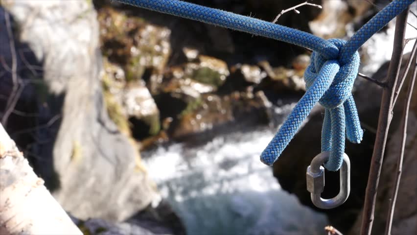 Climbing rope slides in a carabiner and mountain stream in the background