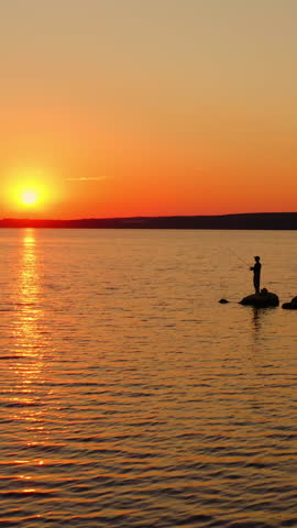 The fisherman fishes at sunset. A fisherman silhouette fishing at sunset. Freshwater fishing, catch of fish. Video from a side. Vertical video
