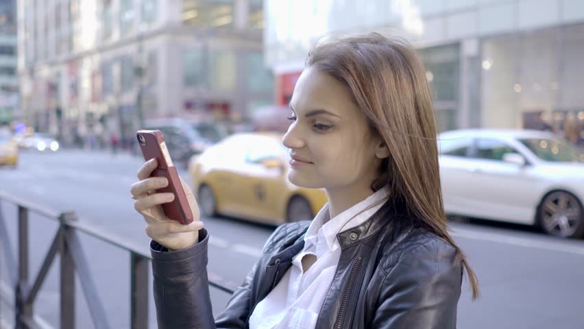 A Young Woman Uses her Smart Phone as She Walks along the City Streets