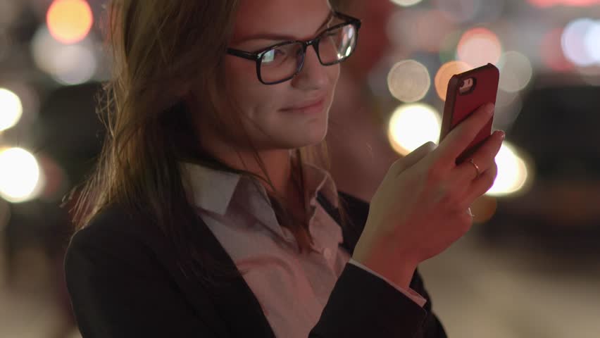 Young Woman Walks through City Streets with Smart Phone in Hand