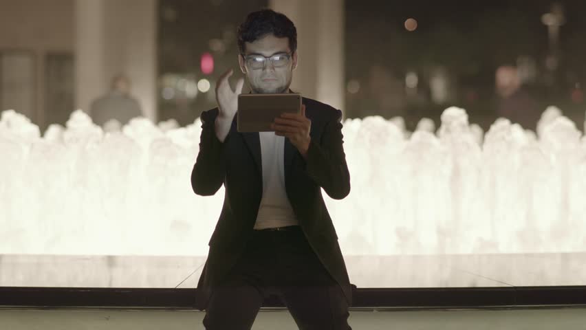 A Gaze of a Man is Fixed upon his Touchpad on a City Nightlife