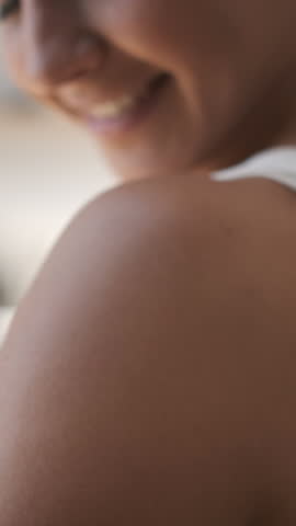 Woman applying skin care cream. Happy smiling young female applying sunscreen or moisturizer lotion on a shoulder. Beauty skin concept. Body care at home interior on a sunny day. Close up 4K