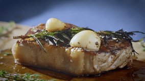 Hot steak on a wooden cutting board. Fried meat with garlic and rosemary. The chef heats the steak with a flame. Slow motion 100fps 4k video.