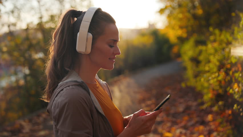 Hello autumn. smiling elegant woman in fitness clothes in the park listening to the music with headphones.