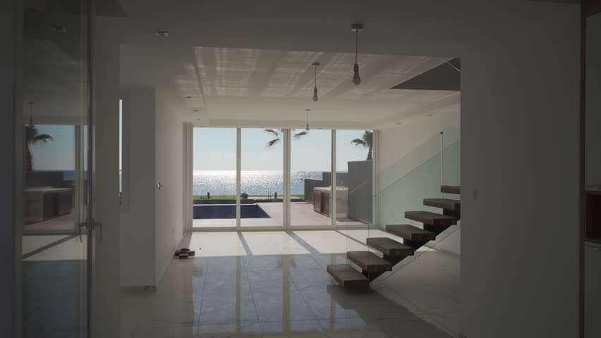 Luxury beachfront villa interior, modern design, floating wooden staircase, marble floors, ocean view, patio access, high-end real estate investment, vacation rental, property market showcase.