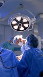 Male neurosurgeon assisted by two doctors performs neurosurgical operation. Main surgeon works under the bright round lamp. Vertical video.