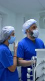 Female nurse talking to a male anesthesiologist in the surgery room. Medics wearing blue uniforms and masks stand talking. Vertical video.