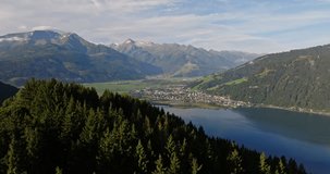Aerial footage from a drone gliding over a dense forest with lush green foliage as it approaches a quaint Austrian town nestled along the shores of a lake surrounded by majestic mountains