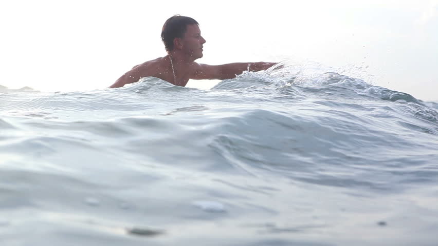 Happy professional surfer swimming on surf board in ocean