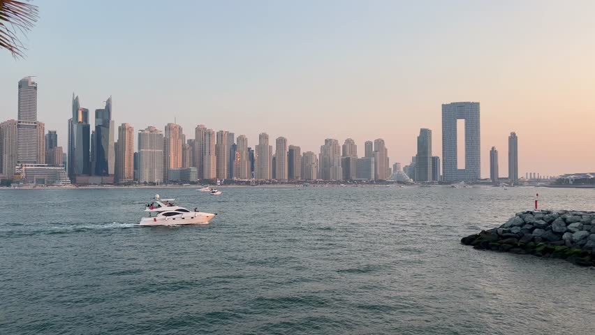 Dubai Jumeirah beach with marina skyscrapers in UAE. Luxurious sandy beach in the Dubai Marina area with views of the iconic skyscrapers. Beaches and Dubai eye view at sunset with boats and yachts.