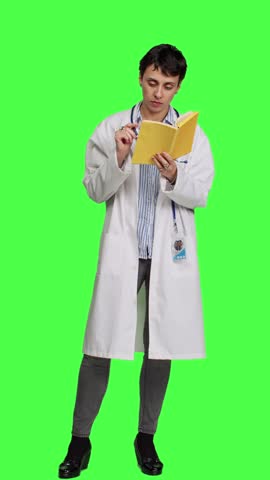Front view Medic specialist reading a healthcare literature book to develop her medical expertise in the industry, stands against greenscreen backdrop. Clever doctor in white coat enjoys lecture Royalty-Free Stock Footage #3467219857