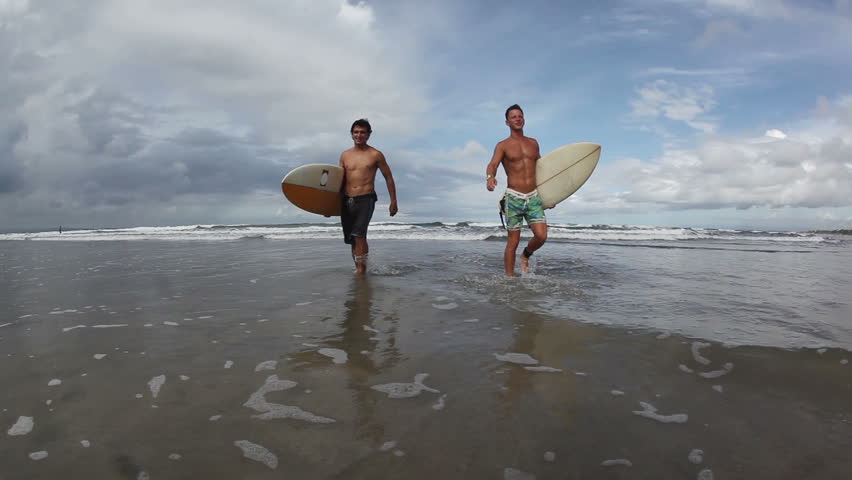 Two happy young surfers holding their surf boards and walking