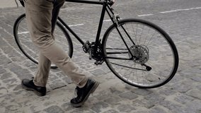 Slow motion video of young man walking on street and getting on old vintage bicycle