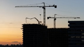 Construction in progress. Time lapse of a breathtaking view to the construction site with silhouettes of cranes and a lot of workers on the sunset sky background. Aerial view - Powered by Shutterstock - Get 15% off with code: PIKWIZARD15