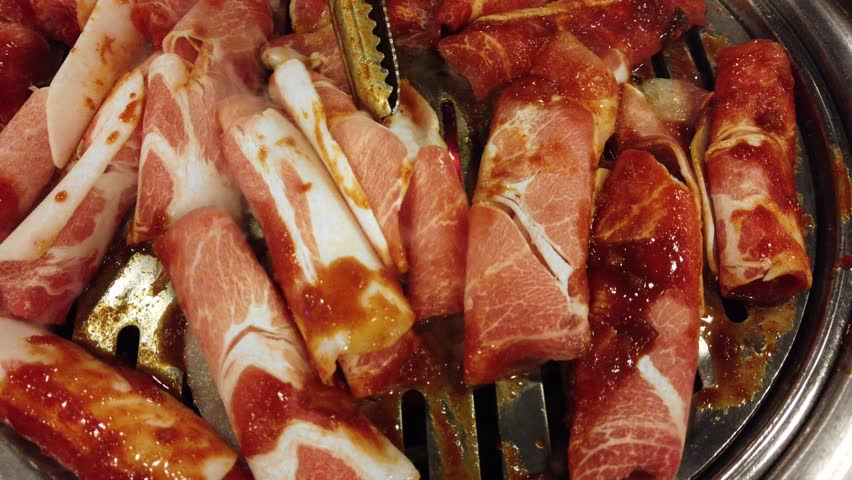 Korean restaurant style BBQ thin curly shaves of frozen beef (Chadolbaegi). Meat smothered with chili paste (gochujang). Surrounded by numerous traditional side dishes. Camera zooms out. 4k60.