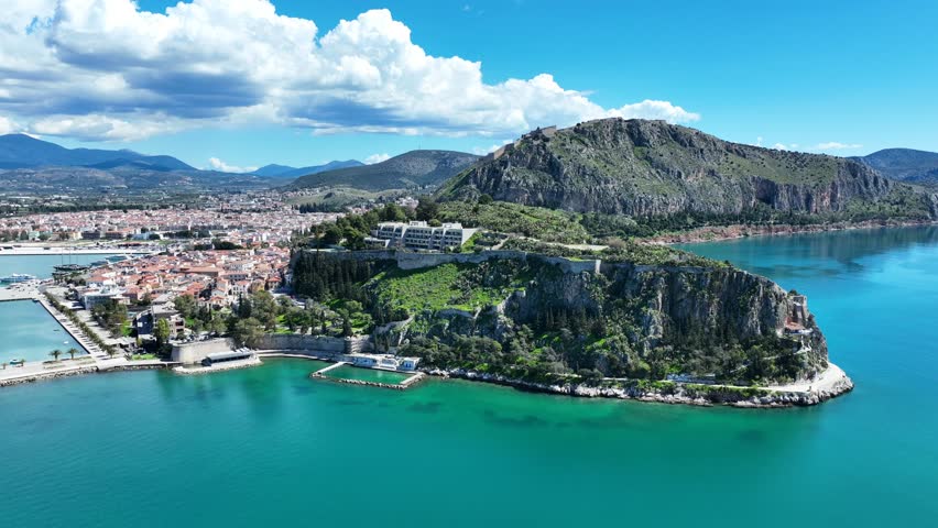 Aerial drone cinematic video of iconic Acronafplia fortress overlooking old city of Nafplio below famous castle of Palamidi as seen at morning with beautiful clouds and deep blue sky, Argolida, Greece