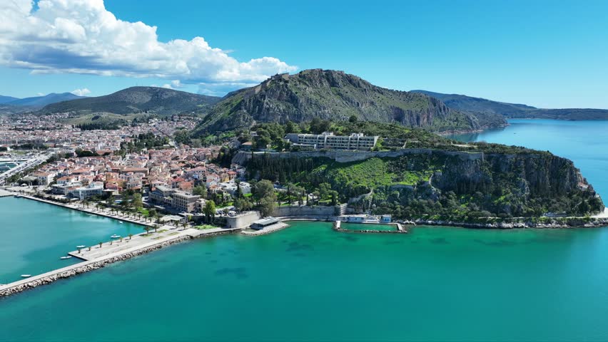 Aerial drone cinematic video of iconic Acronafplia fortress overlooking old city of Nafplio below famous castle of Palamidi as seen at morning with beautiful clouds and deep blue sky, Argolida, Greece