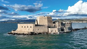 Aerial drone cinematic video of castle of Bourtzi built at sea a popular attraction in city of Nafplio as seen in the morning with nice white clouds and deep blue sky, Argolida, Greece