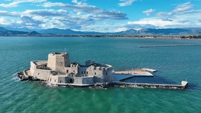 Aerial drone cinematic video of castle of Bourtzi built at sea a popular attraction in city of Nafplio as seen in the morning with nice white clouds and deep blue sky, Argolida, Greece