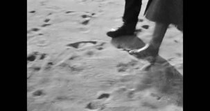 Close up, people feet in boots walk on sea sand. People in autumn walk along sea coast. Walking near seaside landscape. Winter weekend by ocean nature. Vintage black white film. Retro archive 1980s