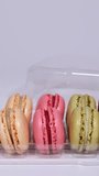 Slow motion of male hand closing a transparent plastic box full of colourful fresh macarons cookies. Traditional french desserts or sweets from almond dough against white background.