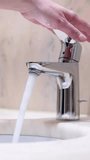 Close-up of caucasian female hand closing a mixer tap in a hotel bathroom. Beautiful fresh and clean water stops running from a shiny chrome faucet into a washbasin. Stop wasting water and energy.