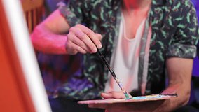 Competent artist wearing green patterned shirt holding paintbrush and palette filled with various colors of paint. Creative art designer moving hand to canvas and making strokes in studio. - Powered by Shutterstock - Get 15% off with code: PIKWIZARD15